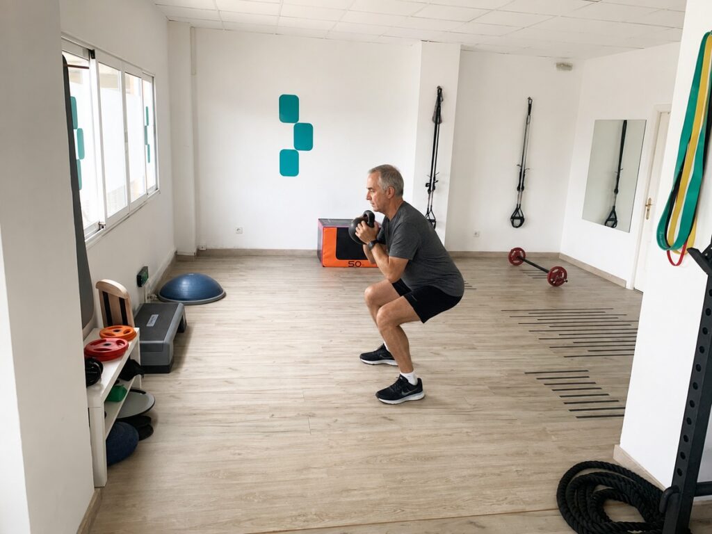 Hombre mayor haciendo sentadilla con kettlebell supervisado en la sala privada de Pila Centro de Entrenamiento, Santander